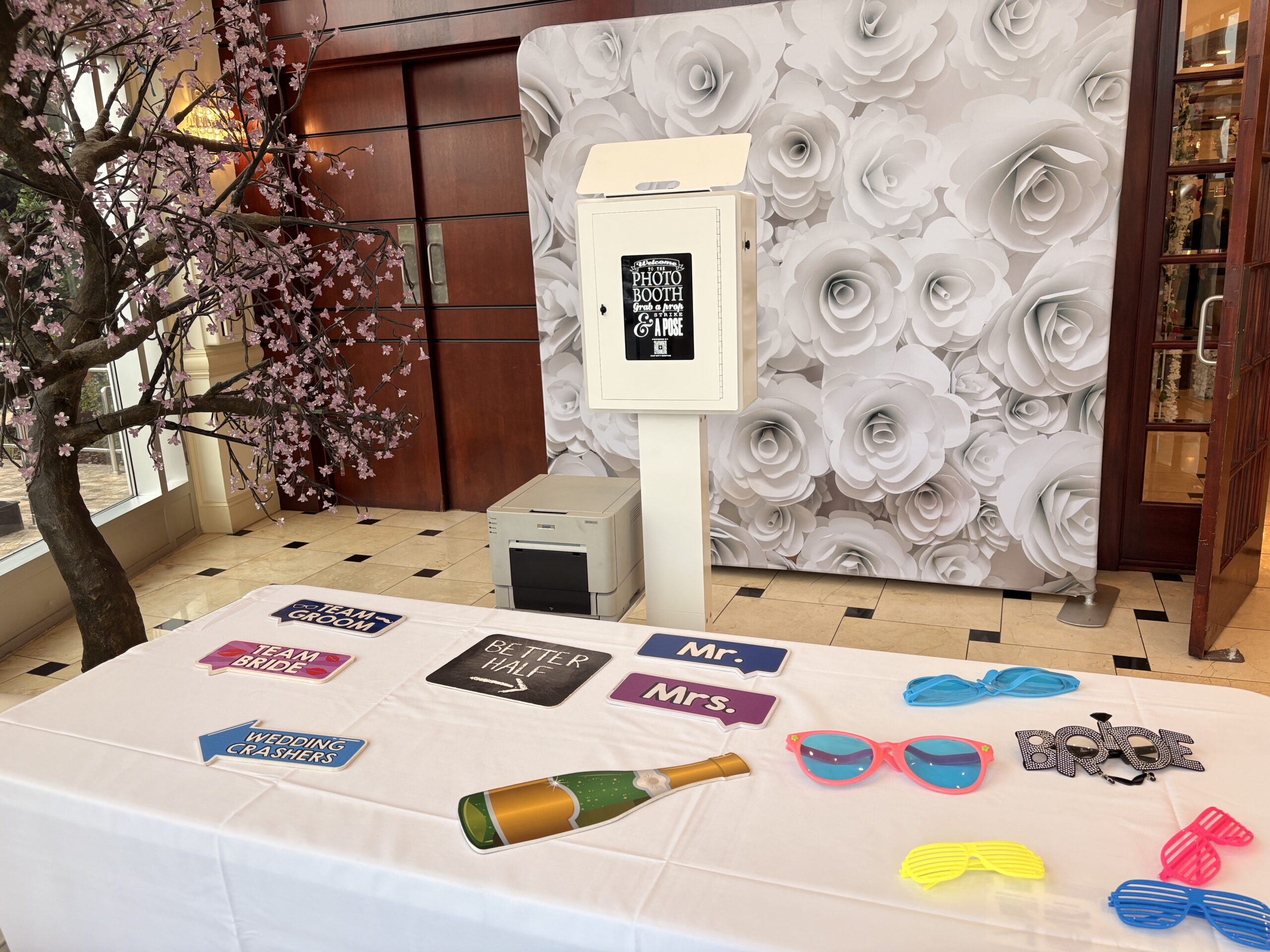 Photo booth with a floral backdrop and props laid out on a table